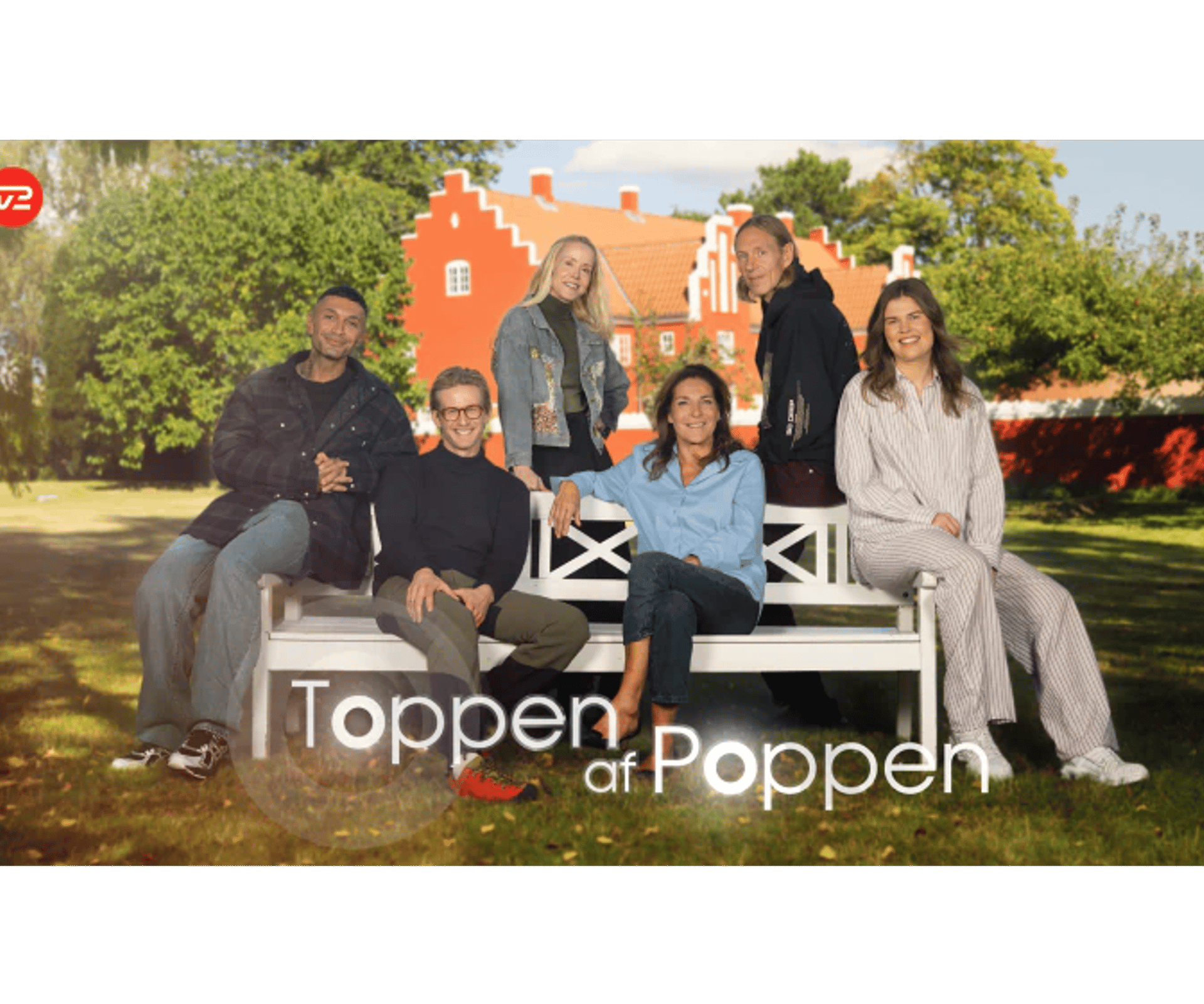 Fem personer sidder og står omkring en hvid bænk i en grøn have foran et rødt hus. Nederst ses teksten Toppen af Poppen og TV2 Play-logoet.