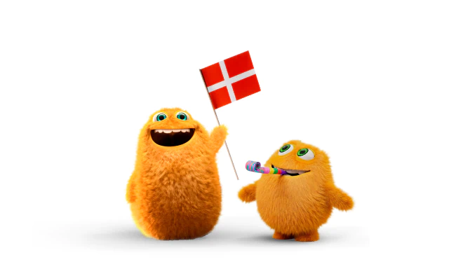 Two fluffy orange cartoon characters are celebrating. One character is joyfully holding a Danish flag, while the other is blowing a party horn. Both have big green eyes and friendly expressions on a white background.
