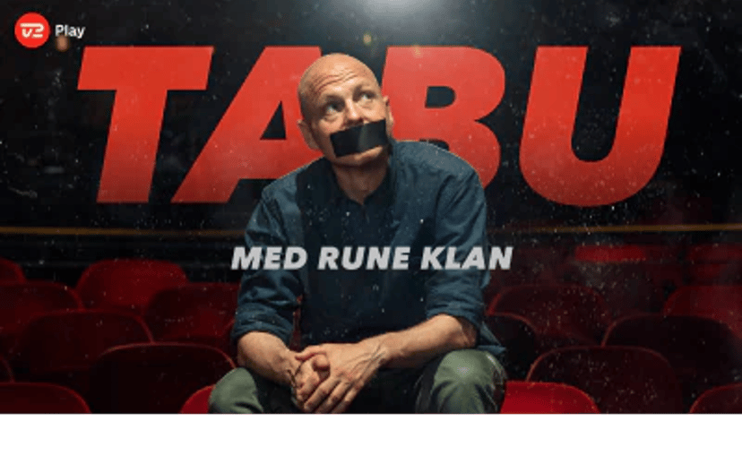 Rune Klan sidder i en biografsal foran den røde titel TABU med en sort mundtape over munden.